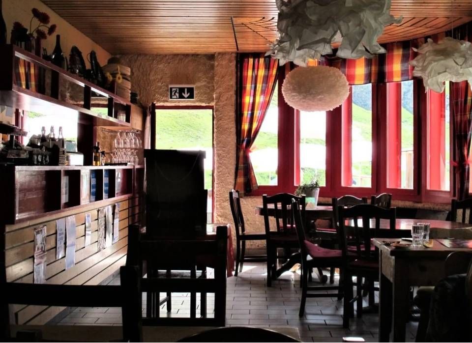 Gemütliches Interieur eines Restaurants mit Holzwänden, Barregalen, dunklen Möbeln und grossen Fenstern mit roten Vorhängen.