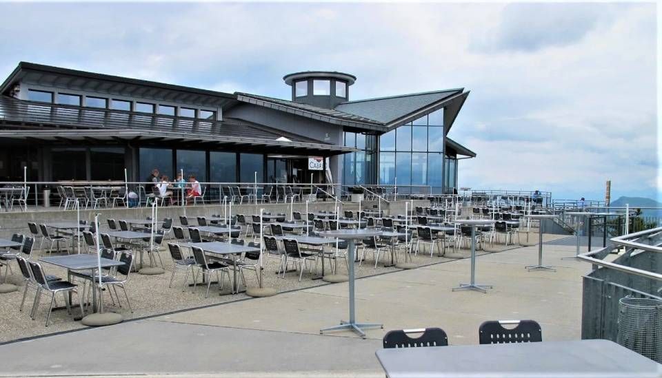 Aussenterrasse mit vielen Tischen und Stühlen vor einem modernen Berggebäude unter bewölktem Himmel.