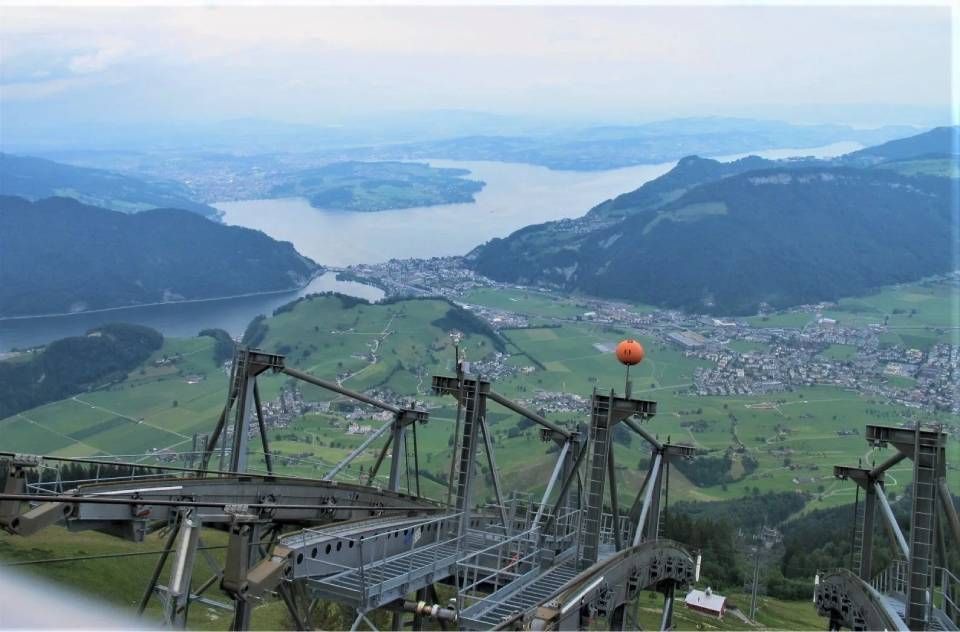 Blick aus der Vogelperspektive auf die Talstation einer Bergseilbahn mit Blick auf einen See und eine Stadt in einem Tal.