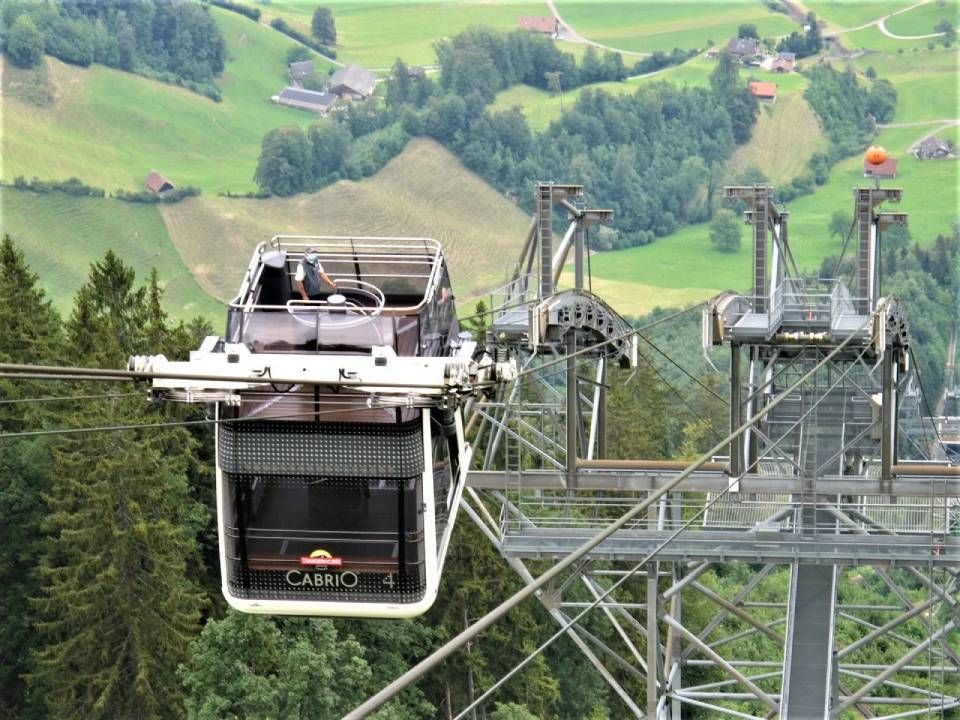 Eine einzigartige, doppelstöckige, offene Seilbahn fährt auf Stahlseilen über eine üppig grüne Berglandschaft.
