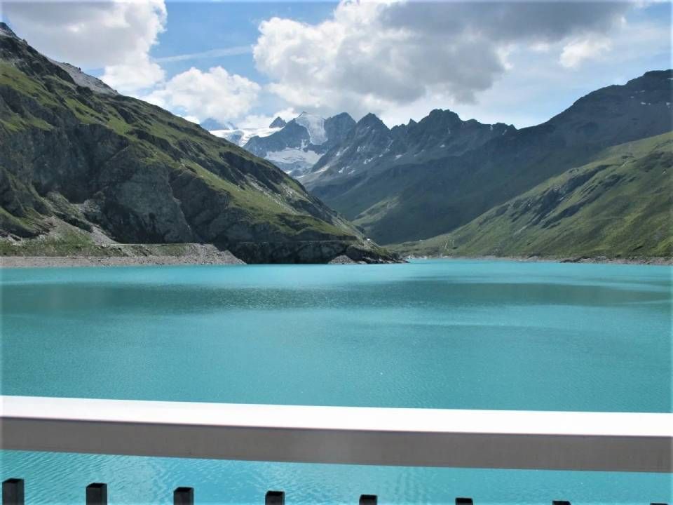 Ein leuchtend türkisfarbener Alpensee, umgeben von steilen, grasbewachsenen Bergen unter einem blauen Himmel mit weissen Wolken.