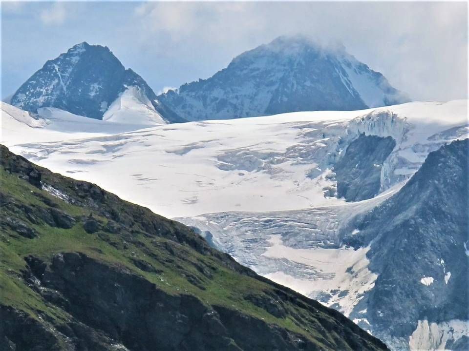 Ein riesiger, schneebedeckter Gletscher, eingebettet zwischen schroffen Berggipfeln unter einem bewölkten Himmel.