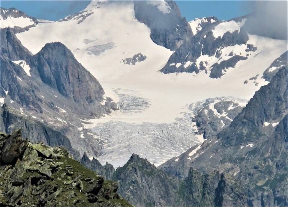 Eine hochgelegene Gebirgslandschaft mit einem riesigen, von Gletscherspalten durchzogenen Gletscher, eingebettet zwischen steilen, zerklüfteten, schneebedeckten Gipfeln.