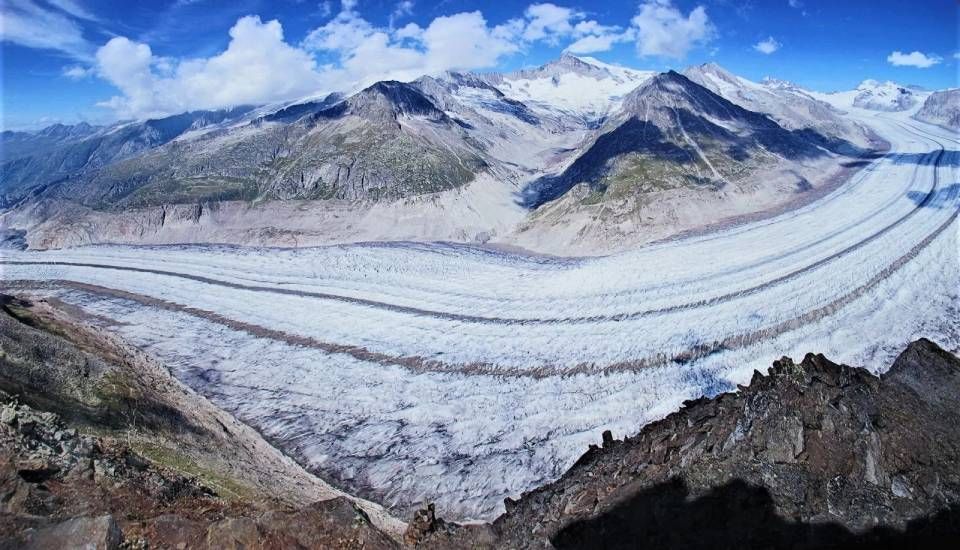 Ein Panoramablick auf den Aletschgletscher in den Schweizer Alpen, der einen sich schlängelnden Eisstrom zeigt, der von Felsmassiven flankiert wird.