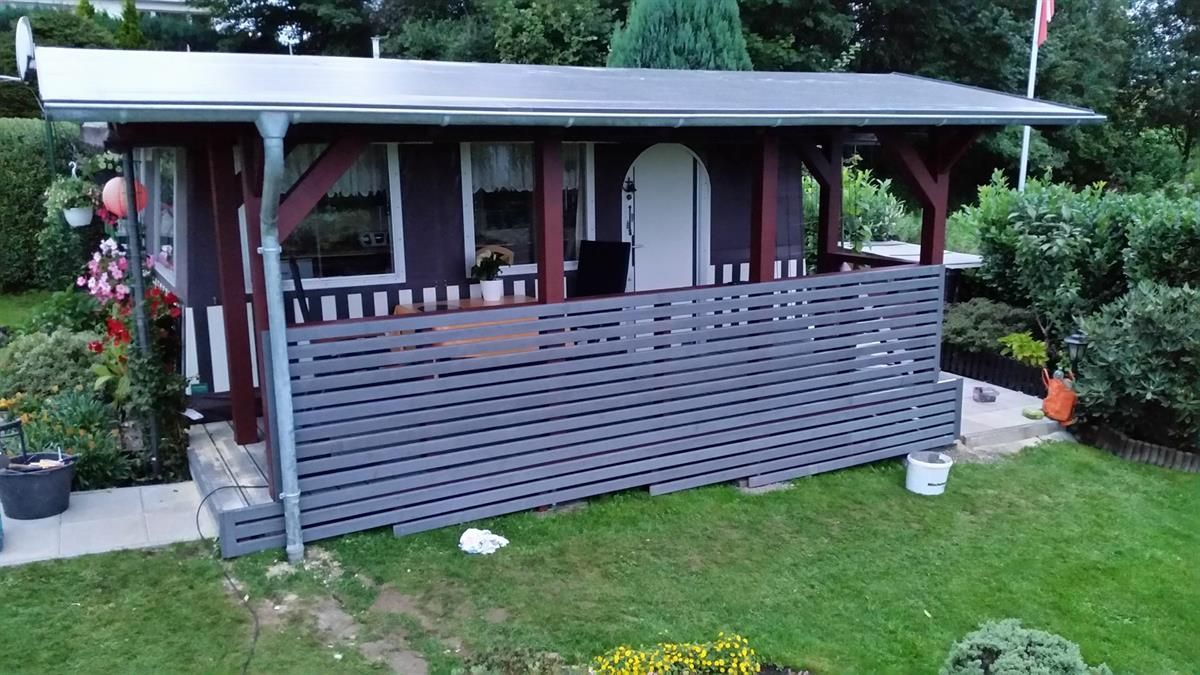 Ein kleines Haus mit einer Veranda inmitten eines Gartens.