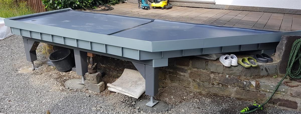 Ein grauer Tisch steht auf einer Kiesfläche neben einer Backsteinmauer.