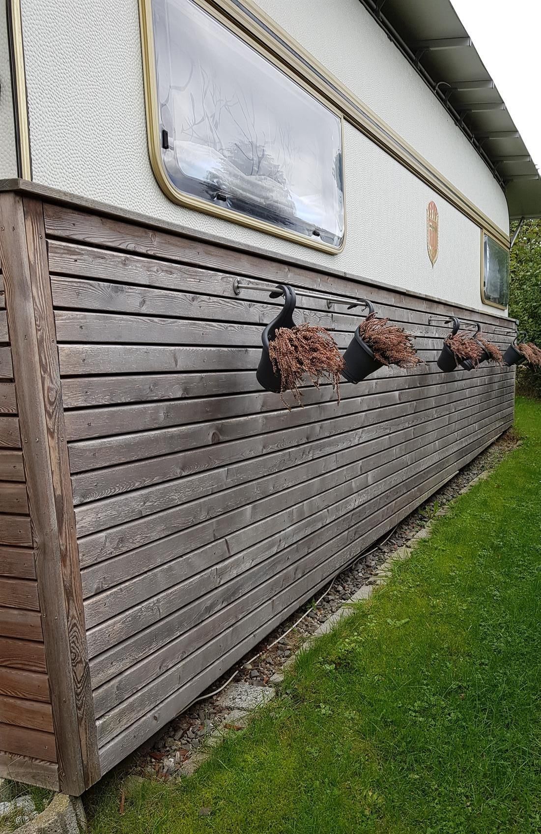 Eine Holzwand mit daran hängenden Topfpflanzen.