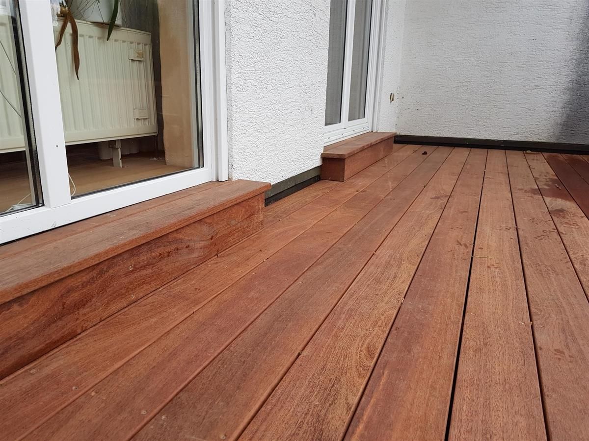 Ein Holzdeck mit einer Glasschiebetür im Hintergrund.