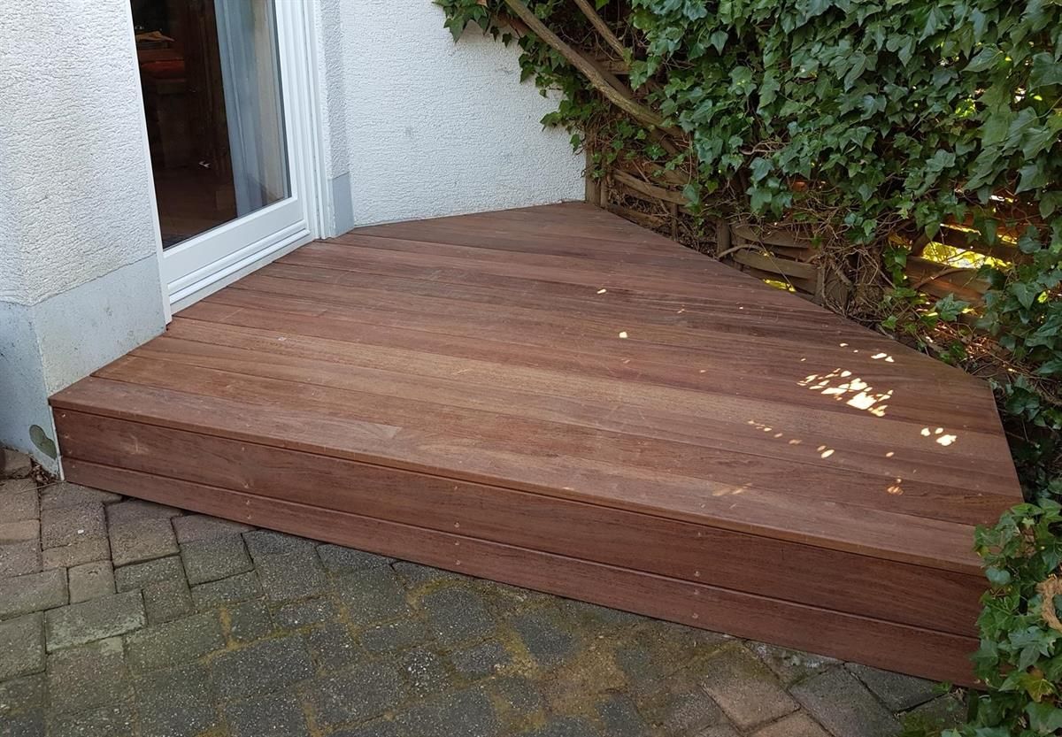 An der Seite eines Gebäudes neben einer Tür liegt ein Holzdeck.