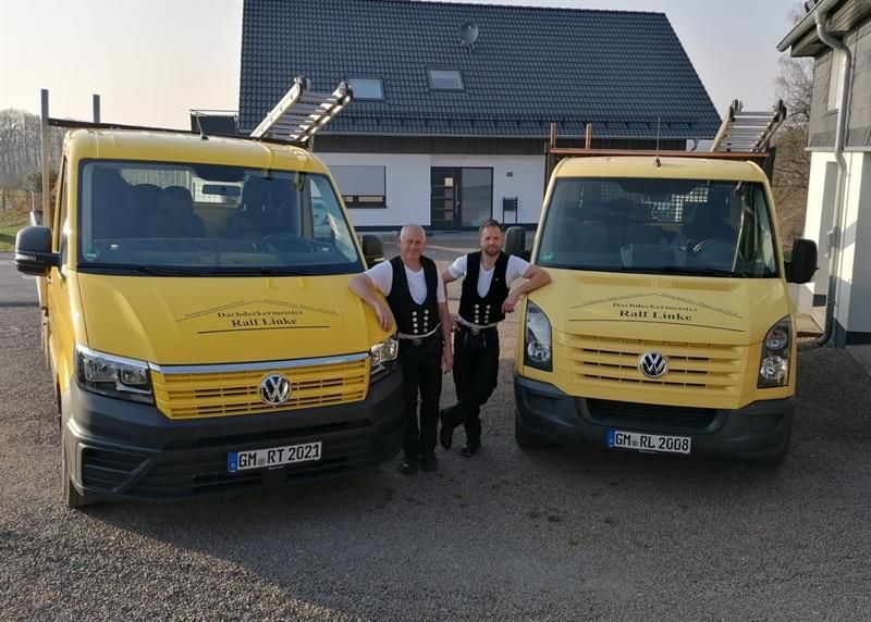 Zwei Männer stehen neben zwei gelben Lieferwagen vor einem Haus.