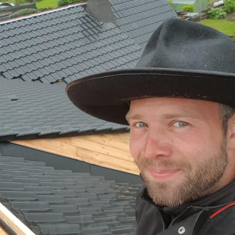 Ein Mann mit Hut steht vor einem Dach