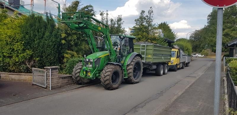Ein grüner Traktor parkt am Straßenrand neben einem LKW.
