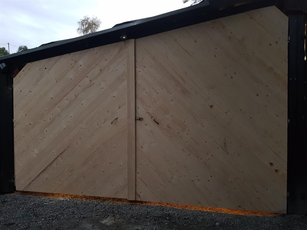 Ein Holzschuppen mit schwarzem Dach und Holztür.