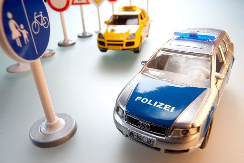 Ein Spielzeugpolizeiauto mit blauen Lichtern steht neben einem gelben Auto und Verkehrsschildern.