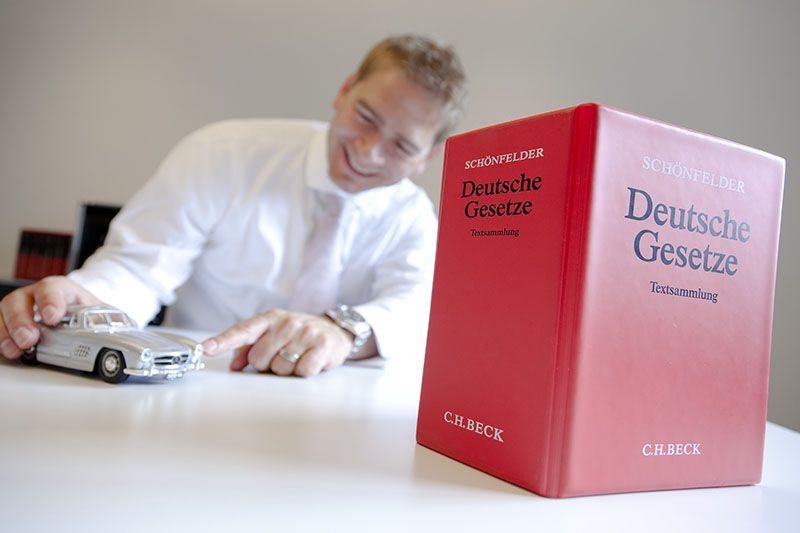 Ein Mann spielt mit einem Spielzeugauto neben einem roten Buch mit dem Titel „Deutsche Gesetze“