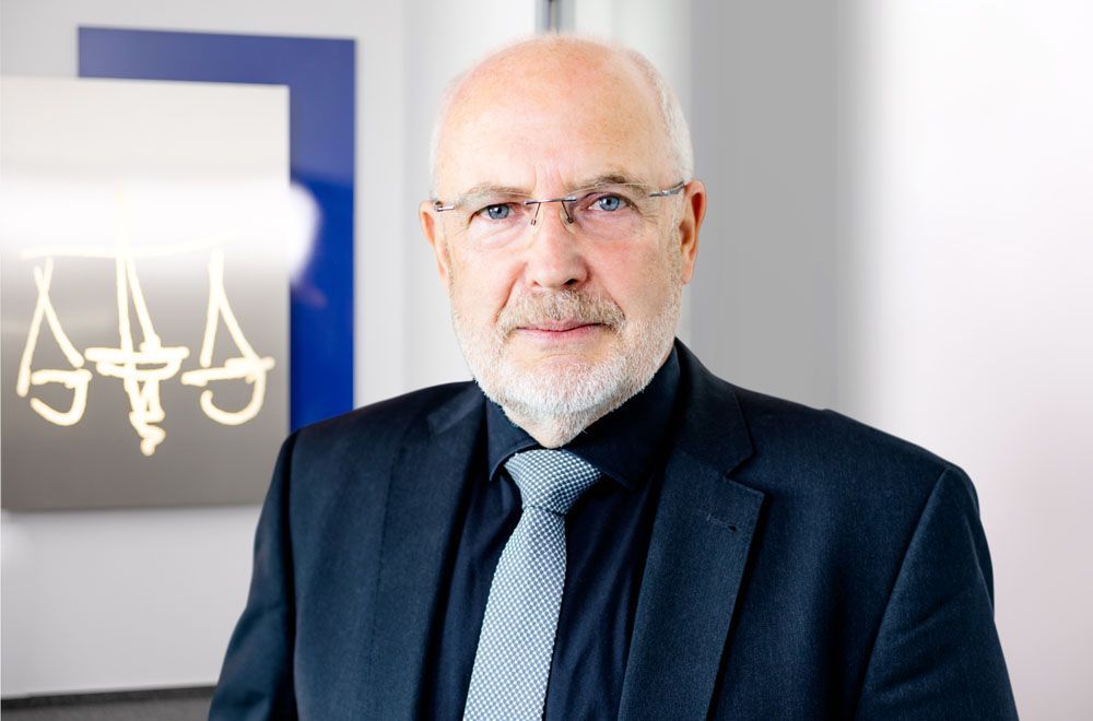 Ein Mann in Anzug und Krawatte steht vor einem Schild mit der Aufschrift „Gerechtigkeit“.