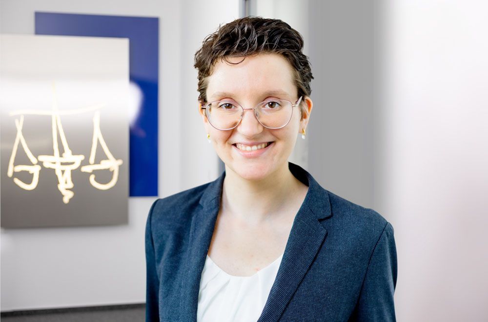 Eine Frau im Anzug lächelt vor einem Schild mit der Aufschrift „Aaa“.