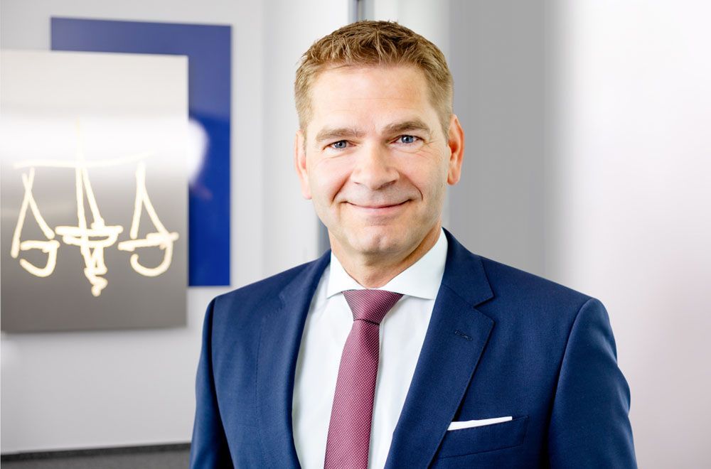 Eine Frau im Anzug lächelt vor einem Schild mit der Aufschrift „Aaa“.