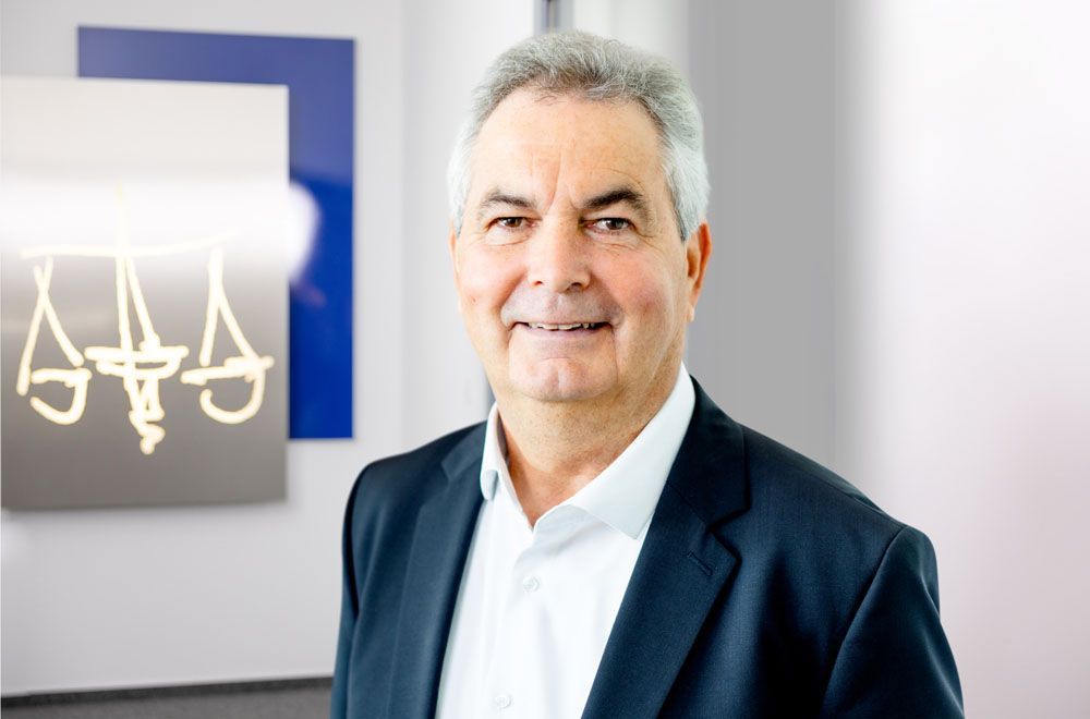 Eine Frau im Anzug lächelt vor einem Schild mit der Aufschrift „Aaa“.