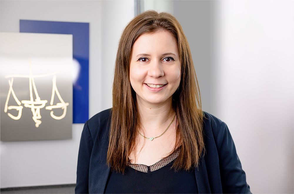 Eine Frau im Anzug lächelt vor einem Schild mit der Aufschrift „Aaa“.