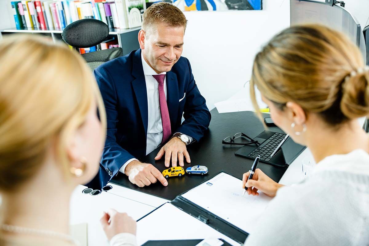 Ein Mann in Anzug und Krawatte sitzt mit zwei Frauen an einem Tisch.