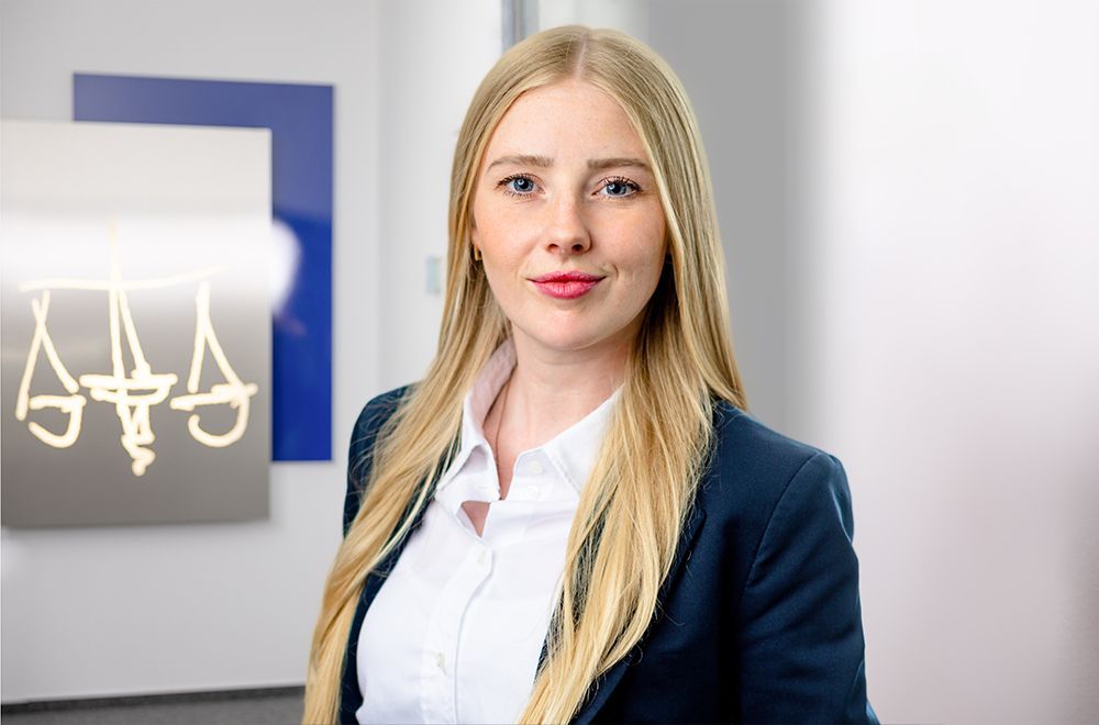 Eine Frau im Anzug lächelt vor einem Schild mit der Aufschrift „Aaa“.