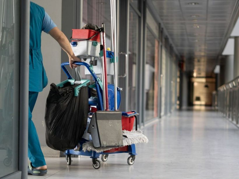 Une femme tire un chariot de nettoyage dans un couloir