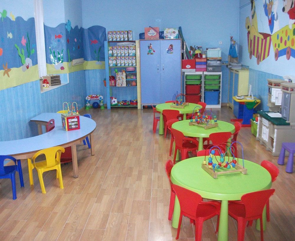 Un aula de preescolar luminosa con mesas, sillas y estantes coloridos, con paredes azules decoradas con obras de arte.