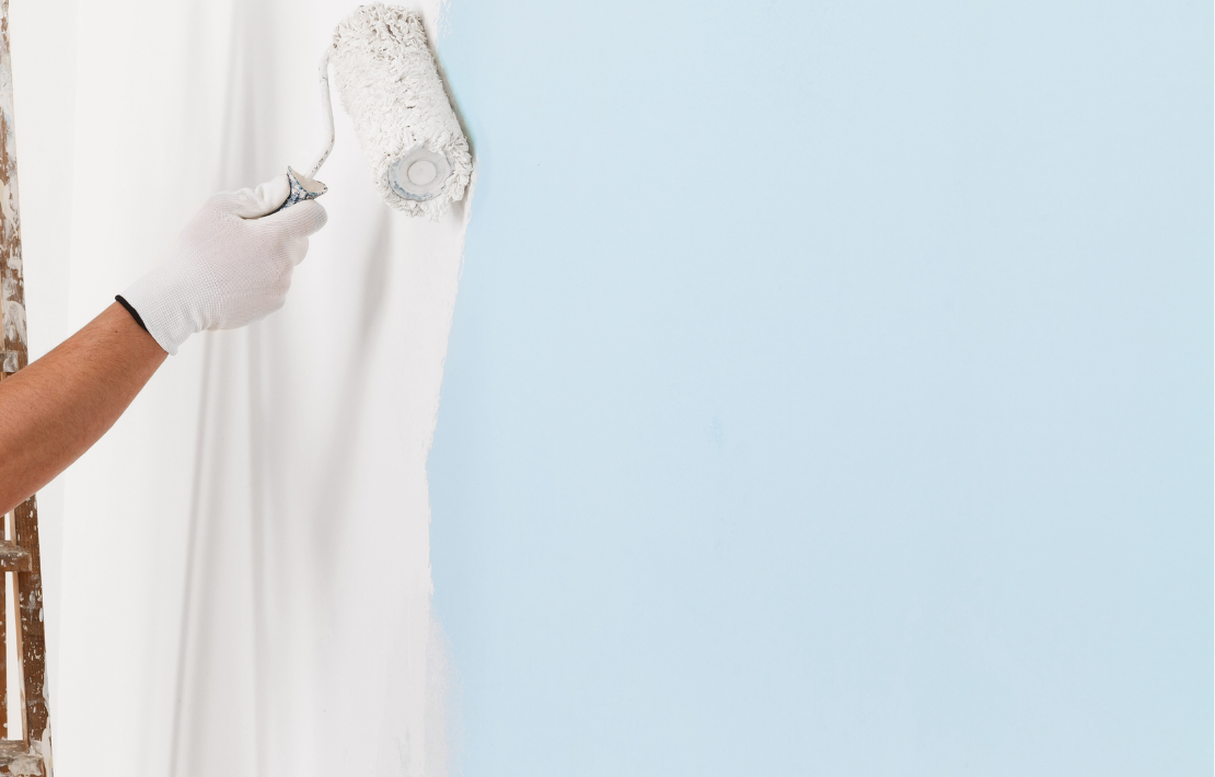 Personne portant un gant utilisant un rouleau à peinture pour peindre un mur en bleu.