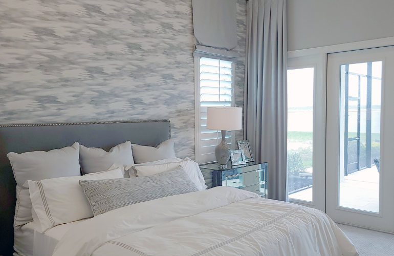 Chambre avec lit, tête de lit bleue, literie blanche, mur d'accent à motifs gris et portes donnant sur l'extérieur.