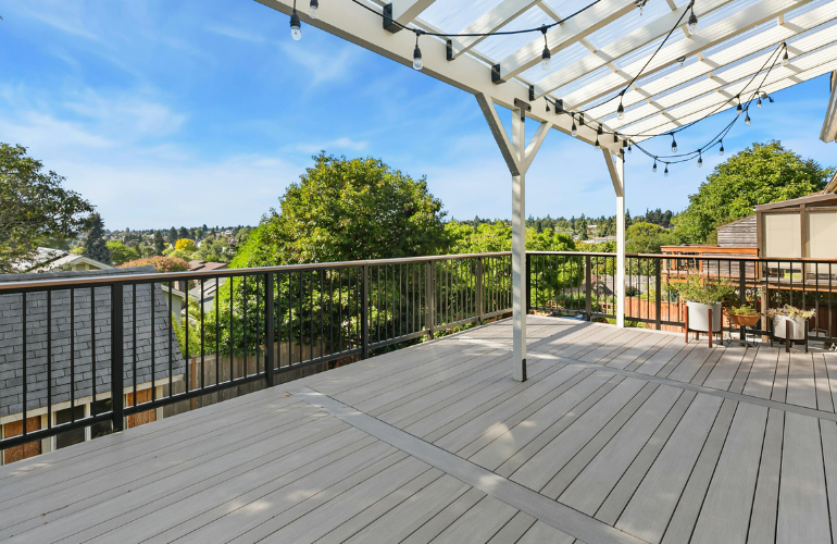 Terrasse avec pergola blanche, balustrades noires et guirlandes lumineuses donnant sur un paysage arboré verdoyant.