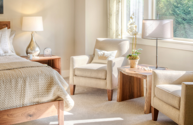 Chambre confortable avec un lit, des fauteuils, des tables de chevet et des lampes.