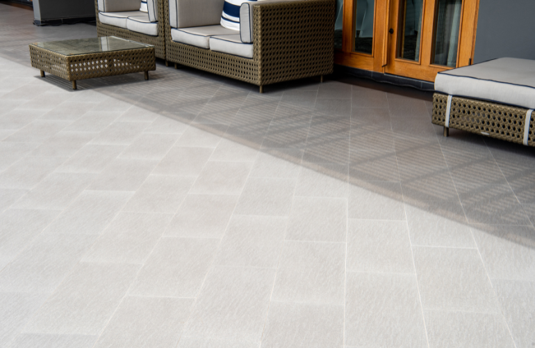 Terrasse extérieure avec sol carrelé gris clair et foncé et mobilier en osier.