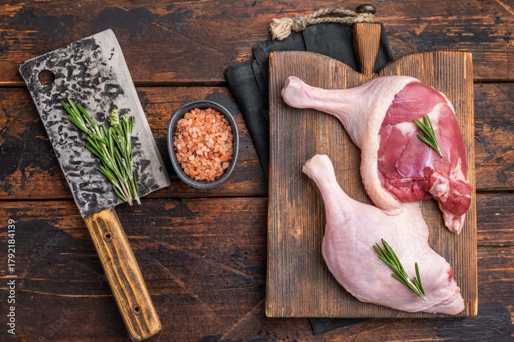 Entenkeulen auf einem Holzbrett mit Hackmesser, Rosmarin und rosa Salz.