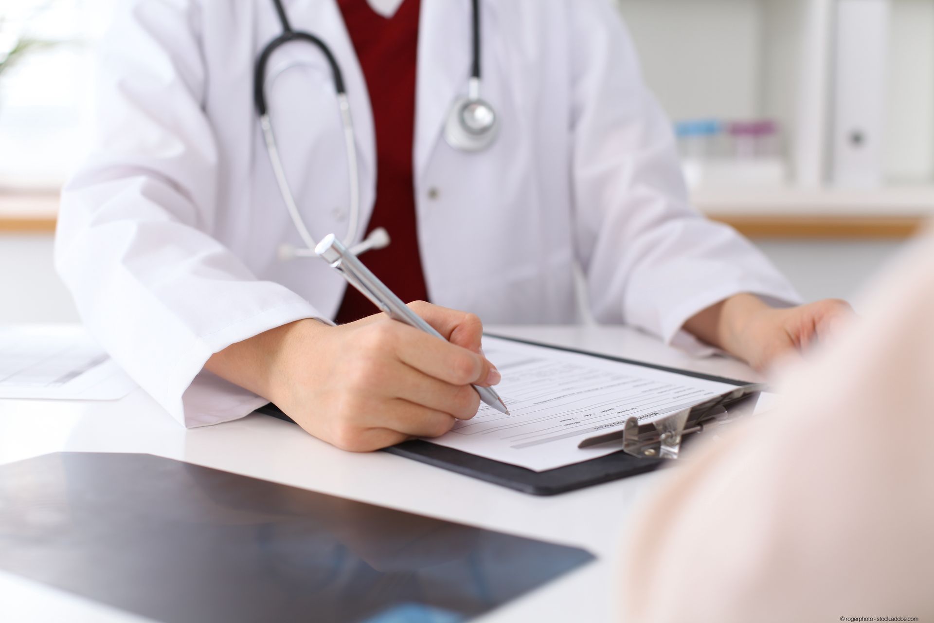 Ein Arzt sitzt an einem Schreibtisch und schreibt auf ein Klemmbrett. Ein Arzt sitzt an einem Schreibtisch und schreibt auf ein Klemmbrett.