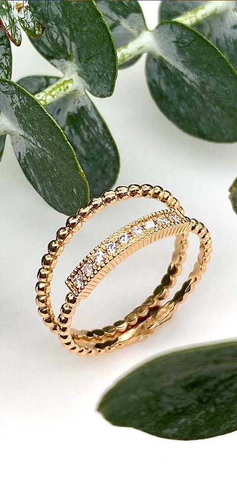 Deux bagues en or, une avec diamants, sur fond blanc avec feuilles vertes.