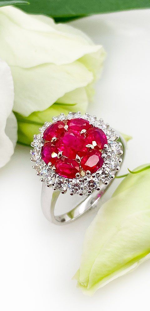 Bague avec pierres précieuses rouges entourées de pierres précieuses blanches et de pétales de fleurs blanches.