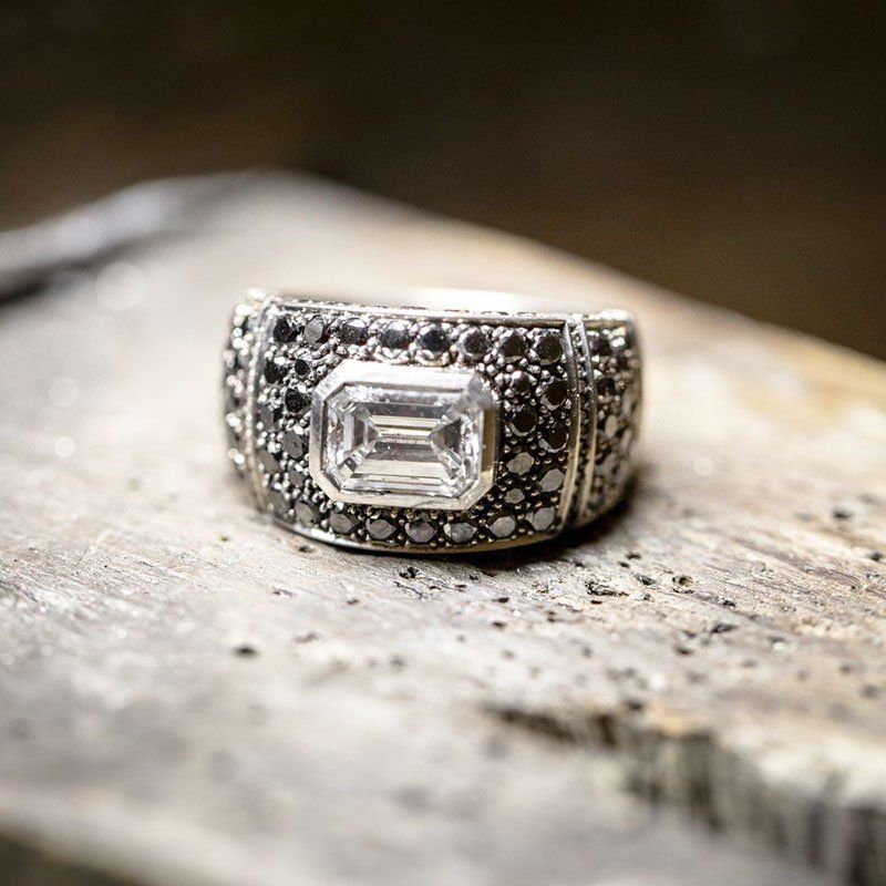 Bague en argent avec pierre centrale blanche taille émeraude sur une surface en bois texturée.