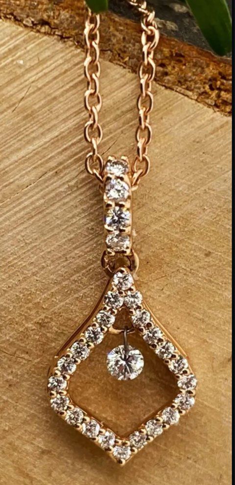 Collier en or rose avec pendentif diamant sur fond bois.