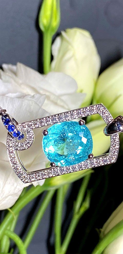 Un pendentif en pierre précieuse turquoise avec des diamants blancs sur une fleur blanche.