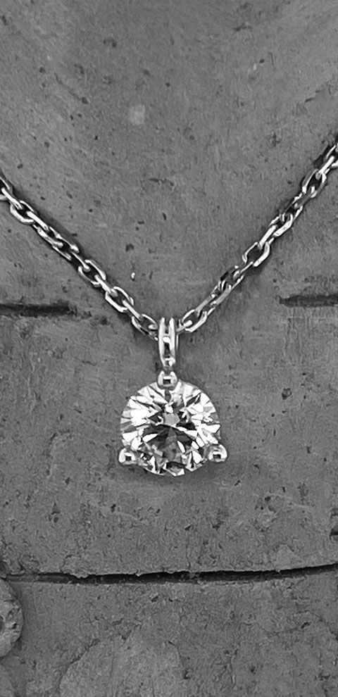 Un collier pendentif en diamant sur une chaîne sur une surface grise texturée.