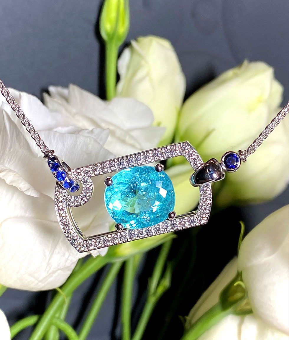 Collier avec une pierre précieuse ovale bleu clair et des diamants environnants, sertis sur fond de fleurs blanches.