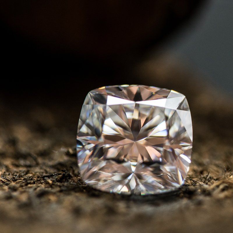 Diamant taille coussin, scintillant, reposant sur une surface marron texturée à fond sombre.