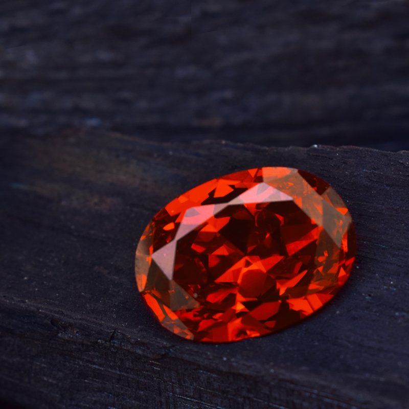 Pierre précieuse orange ardente de taille ovale sur une surface sombre et texturée, réfléchissant la lumière.