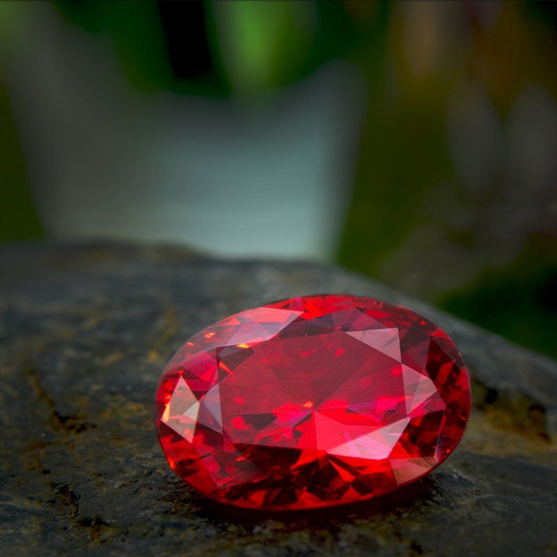 Rubis rouge de taille ovale posé sur une surface rocheuse sombre et texturée.