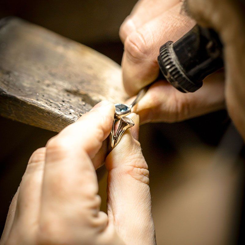Bijoutier travaillant sur une bague en or avec une pierre précieuse bleue, utilisant des outils pour l'affiner.