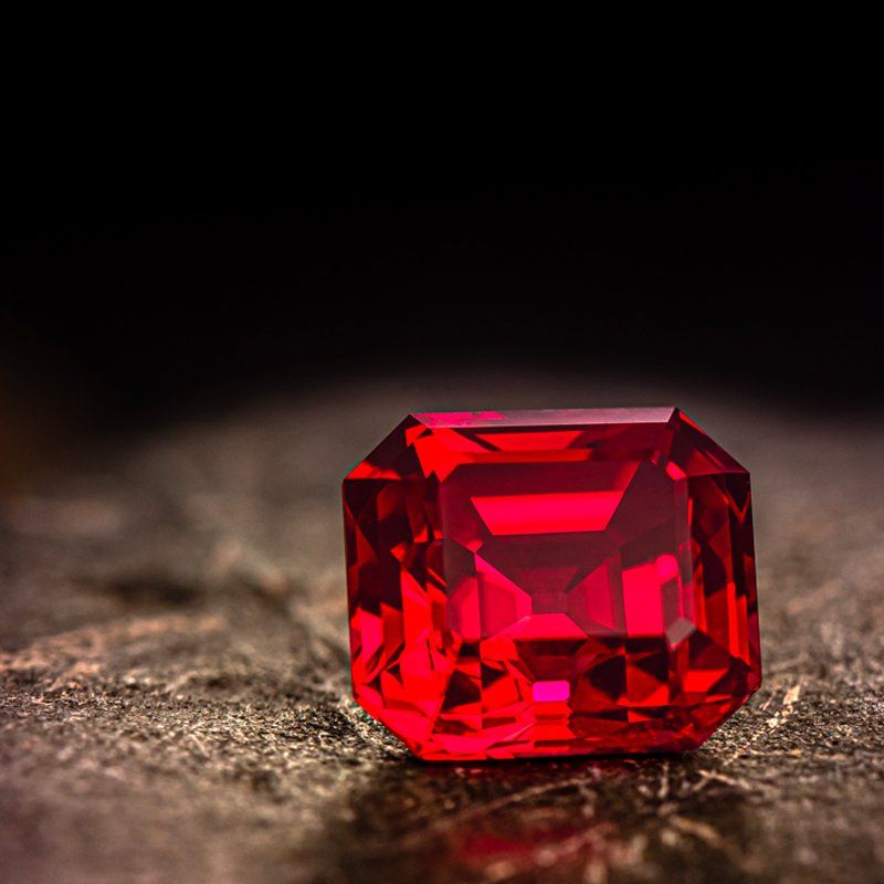 Pierre précieuse rouge taille émeraude sur une surface rugueuse et texturée, fond noir.