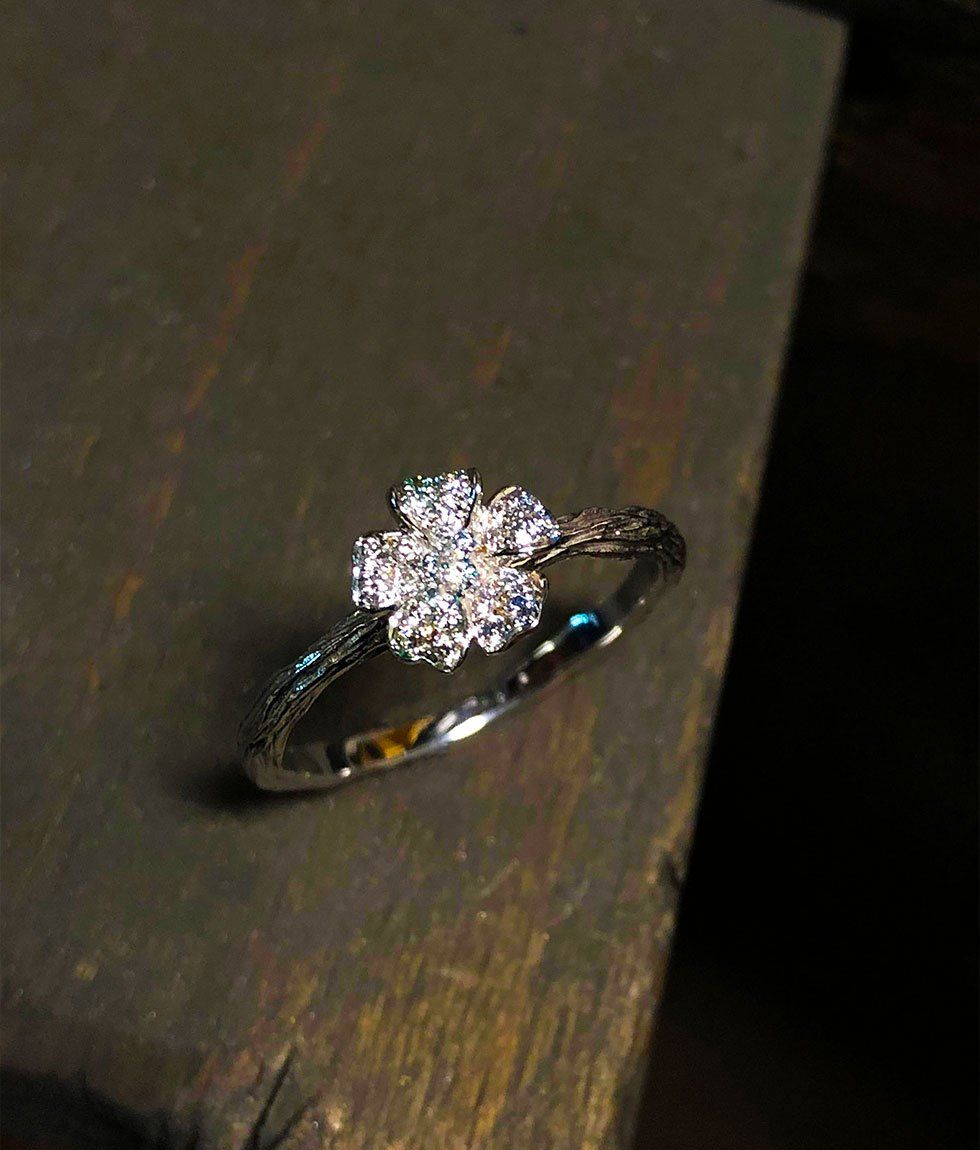 Bague fleur en diamant sur une bande en argent texturée, reposant sur une surface en bois foncé.