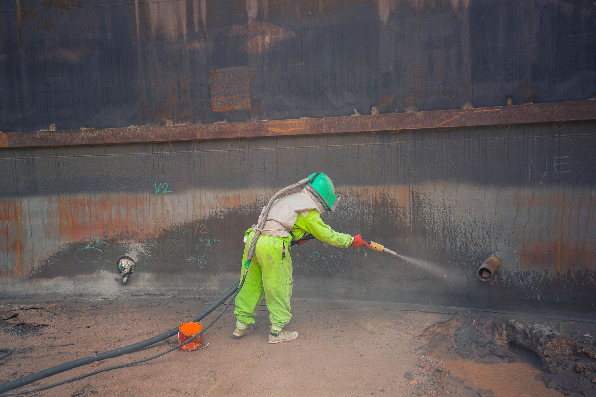 Ein Mann in einem grünen Overall spritzt mit einem Schlauch eine Wand ab, Bröcking Umweltdienste GmbH