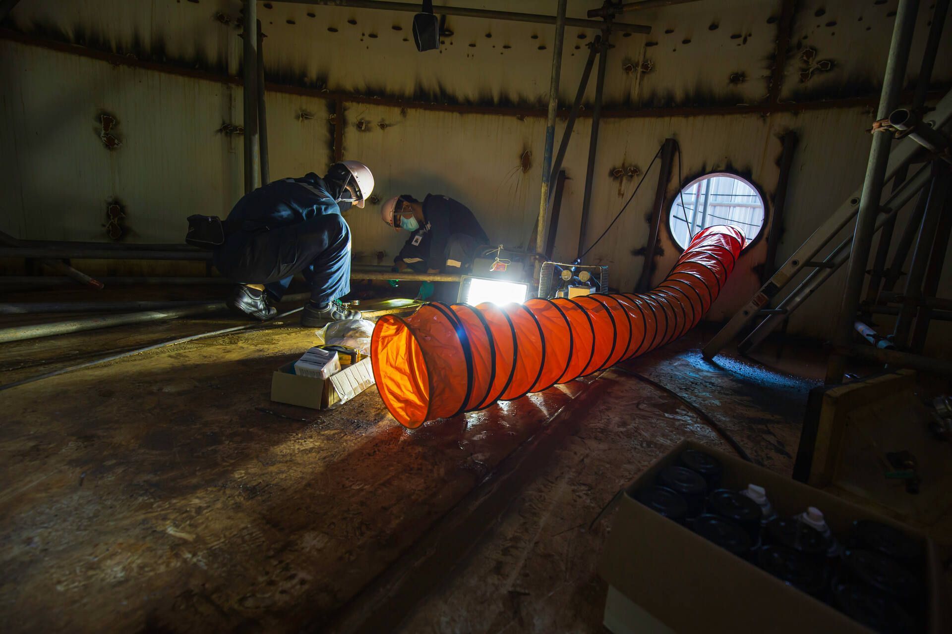 Zwei Männer arbeiten in einem dunklen Raum an einem großen orangefarbenen Schlauch, Bröcking Umweltdienste GmbH